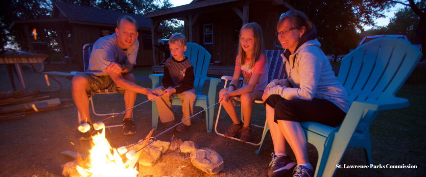Family of four roasting marshmallows on open fire while camping